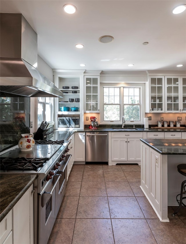 kitchen with glass insert cabinets, wall chimney range hood, white cabinets, a sink, and stainless steel appliances