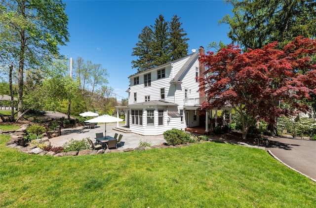 rear view of house featuring a patio, a lawn, a balcony, and a chimney