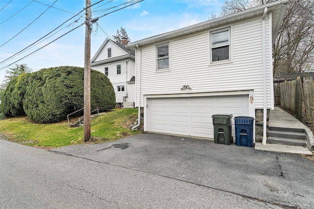 exterior space featuring driveway, a garage, fence, and a front lawn