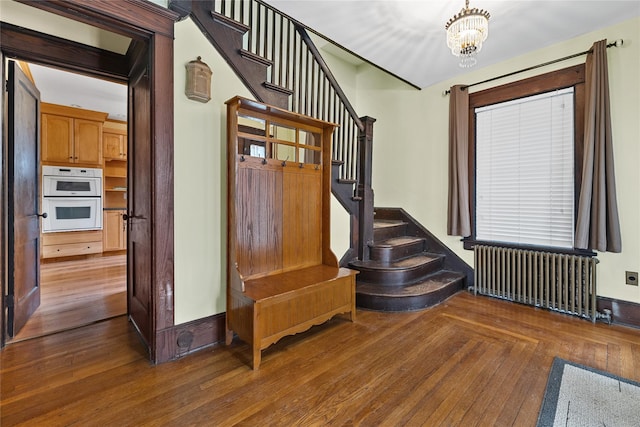 stairs with wood-type flooring, baseboards, radiator, and an inviting chandelier