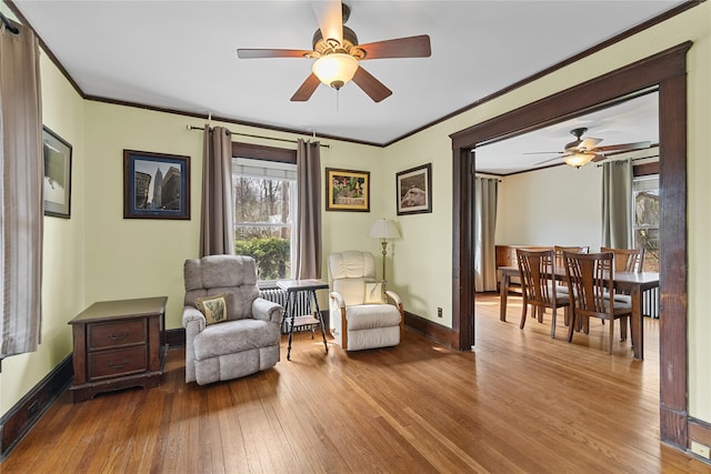 living area featuring baseboards, hardwood / wood-style flooring, a ceiling fan, and ornamental molding