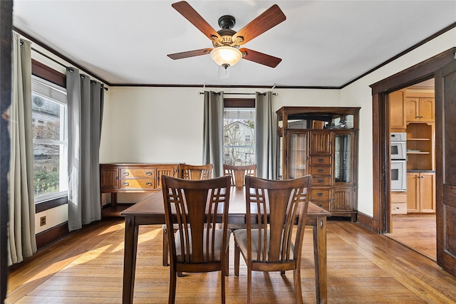 dining space with light wood-style flooring, baseboards, a ceiling fan, and ornamental molding