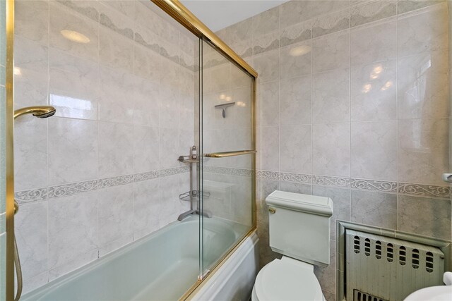 bathroom featuring toilet, radiator, bath / shower combo with glass door, and tile walls