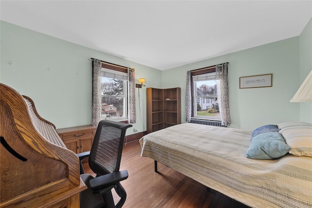 bedroom featuring multiple windows, baseboards, radiator, and wood finished floors