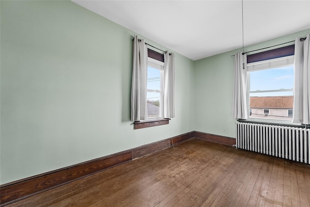 empty room featuring baseboards, radiator, plenty of natural light, and dark wood finished floors