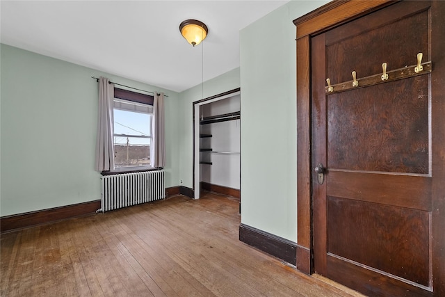 unfurnished bedroom featuring wood-type flooring, baseboards, radiator, and a closet