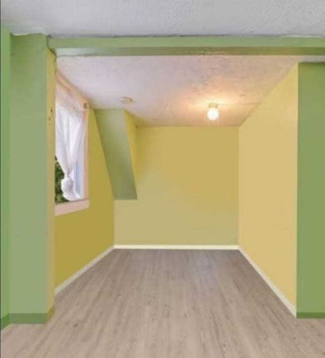additional living space with a textured ceiling, baseboards, and wood finished floors