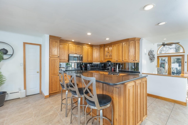 kitchen with a kitchen breakfast bar, recessed lighting, stainless steel microwave, dark countertops, and brown cabinets