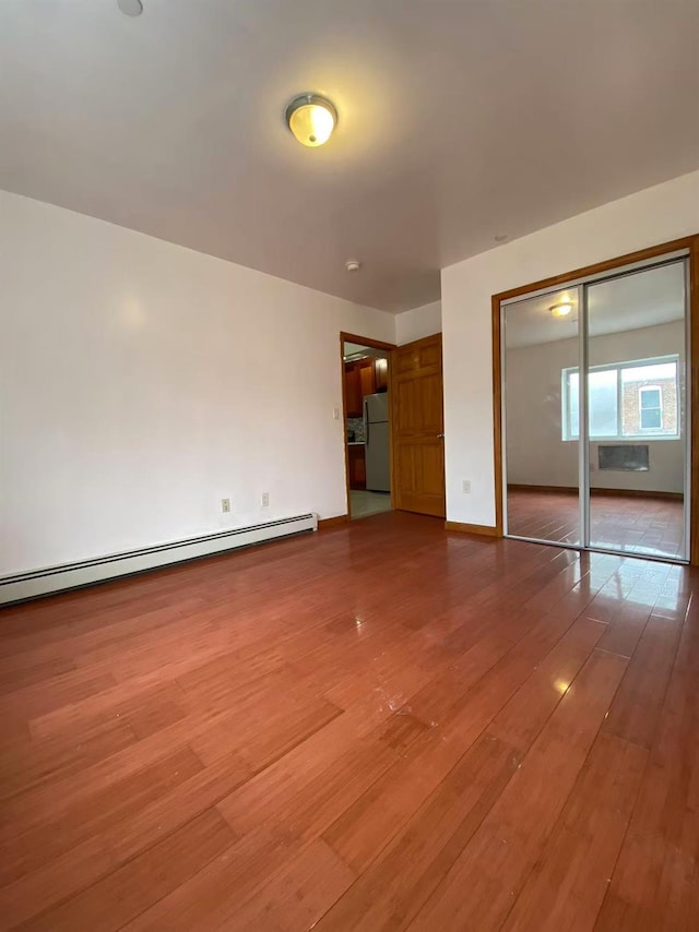 4239 Judge St Unit 2A, Elmhurst, NY 11373 - unfurnished bedroom featuring freestanding refrigerator, baseboard heating, wood-type flooring, a closet, and baseboards