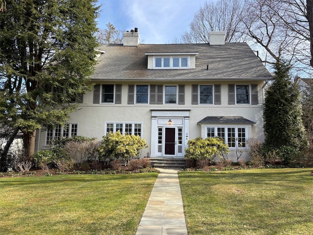 view of front of house with stucco siding, a chimney, and a front lawn