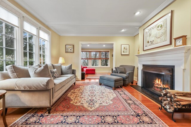 living room featuring wood finished floors, a glass covered fireplace, baseboards, ornamental molding, and recessed lighting