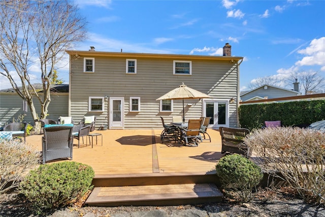 rear view of house featuring french doors, a chimney, outdoor dining area, and a deck