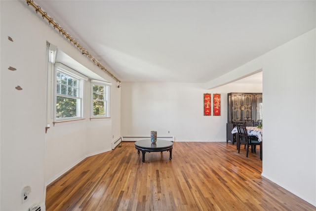 living area featuring a baseboard heating unit, baseboards, and light wood-style flooring