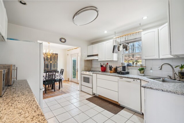 kitchen featuring under cabinet range hood, an inviting chandelier, a sink, white appliances, and decorative backsplash