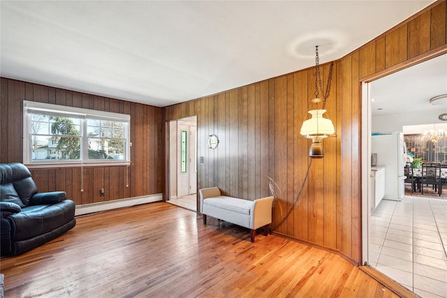 living area featuring baseboard heating, light wood finished floors, baseboards, wood walls, and a notable chandelier
