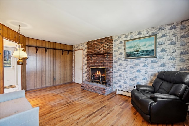 living area with a baseboard heating unit, wallpapered walls, a brick fireplace, and light wood finished floors