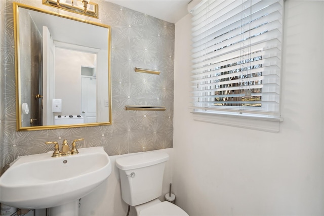half bath with toilet, a sink, and wallpapered walls