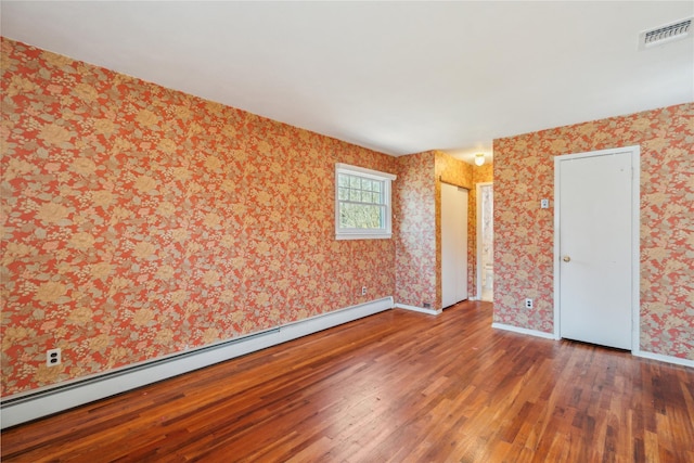 spare room with wallpapered walls, wood finished floors, visible vents, a baseboard heating unit, and baseboards