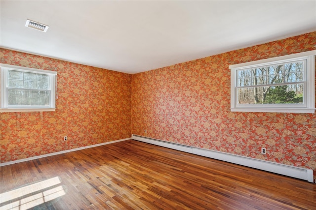 spare room featuring a baseboard heating unit, plenty of natural light, visible vents, and hardwood / wood-style flooring