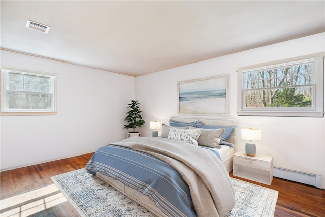 bedroom featuring wood finished floors, visible vents, and a baseboard radiator