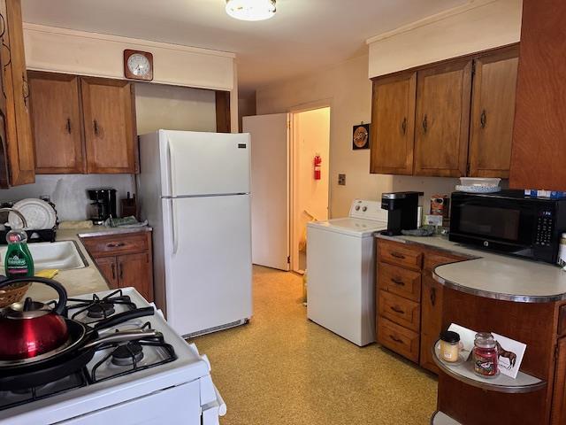 kitchen with brown cabinetry, white appliances, a sink, and washer / clothes dryer