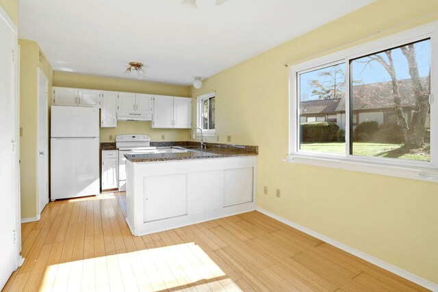 kitchen featuring white appliances, a peninsula, white cabinetry, under cabinet range hood, and baseboards