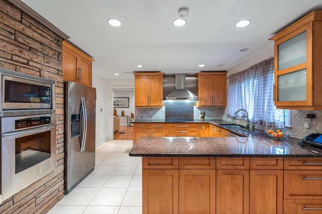 kitchen featuring a peninsula, wall chimney exhaust hood, stainless steel appliances, a sink, and light tile patterned floors