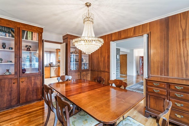 dining room featuring ornamental molding, wood walls, a chandelier, and wood finished floors