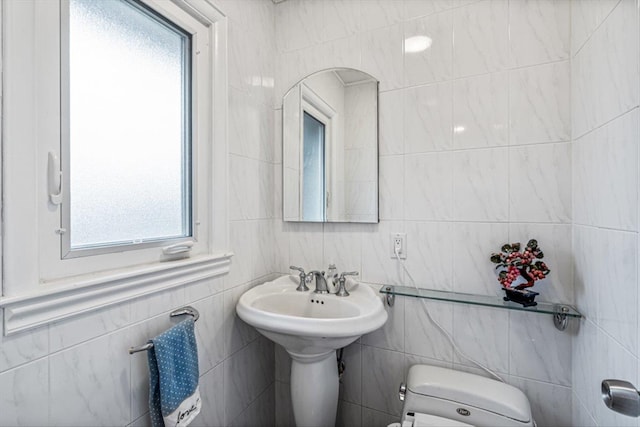 half bathroom featuring tile walls, toilet, and a sink