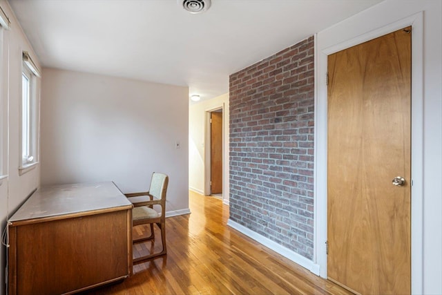 office area featuring baseboards, visible vents, brick wall, and wood finished floors