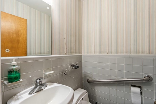 bathroom featuring a sink, tile walls, wallpapered walls, and toilet