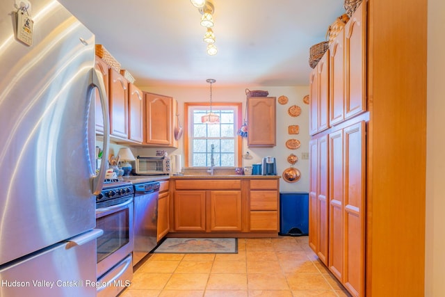 kitchen featuring a toaster, appliances with stainless steel finishes, a sink, hanging light fixtures, and light tile patterned floors