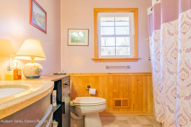 full bath featuring a wainscoted wall, toilet, vanity, wood walls, and visible vents