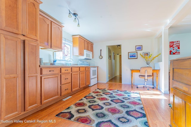 kitchen featuring light countertops, light wood finished floors, baseboards, white appliances, and a sink