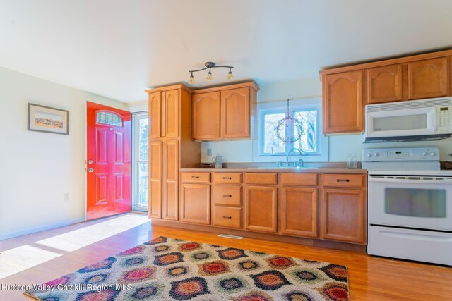 kitchen featuring white appliances, baseboards, a sink, light wood finished floors, and visible vents