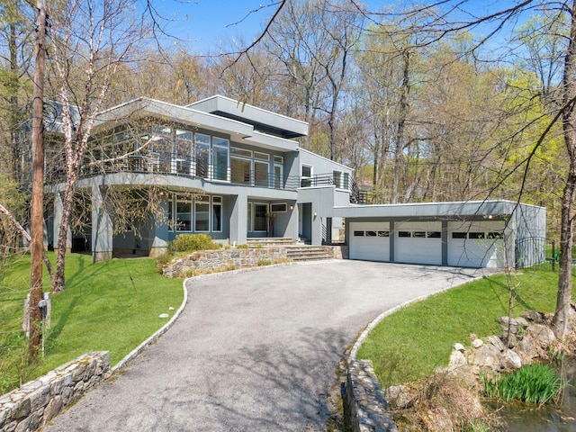 view of front of property featuring driveway, a front yard, a garage, a balcony, and stucco siding
