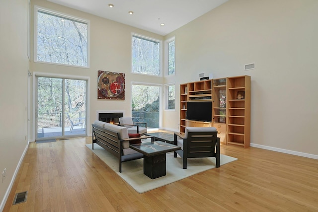 living area featuring a towering ceiling, baseboards, light wood-style flooring, and visible vents
