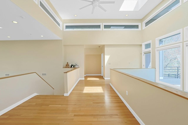 hallway with a towering ceiling, baseboards, recessed lighting, light wood-style flooring, and a skylight