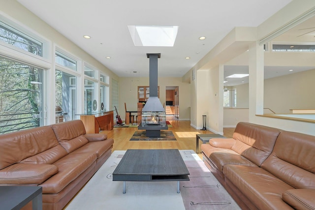 living room with recessed lighting, a skylight, light wood-style flooring, and a wood stove