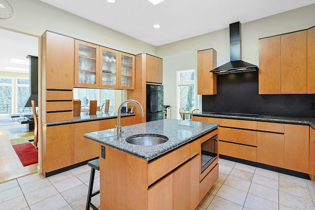 kitchen with a sink, wall chimney exhaust hood, dark stone counters, decorative backsplash, and black appliances