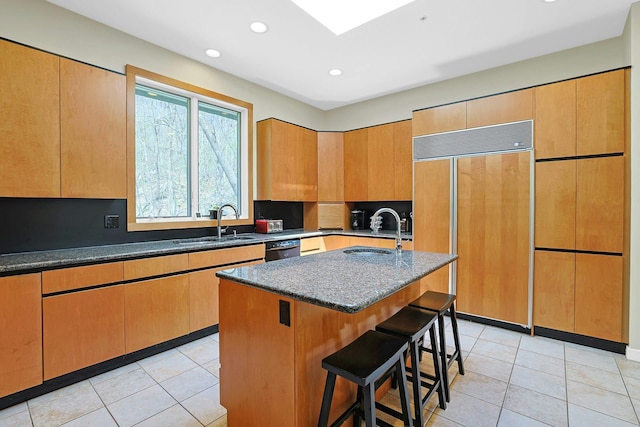 kitchen with paneled built in fridge, a sink, dark stone counters, and a kitchen breakfast bar