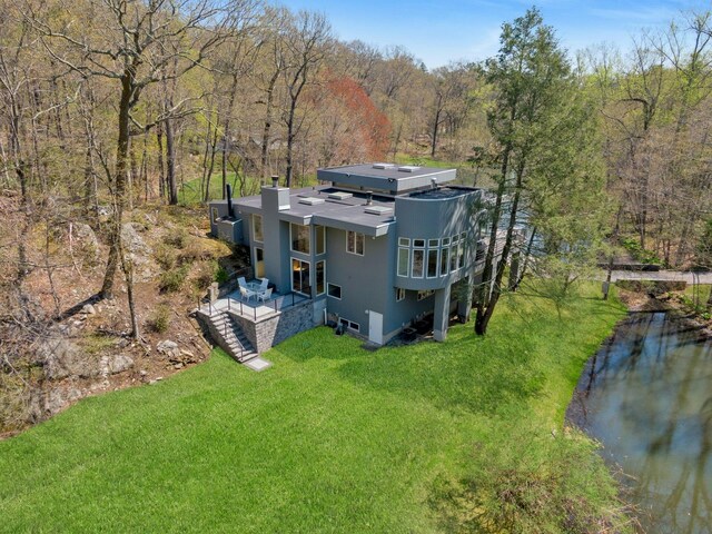 rear view of property with stucco siding, a chimney, a lawn, a water view, and a wooded view