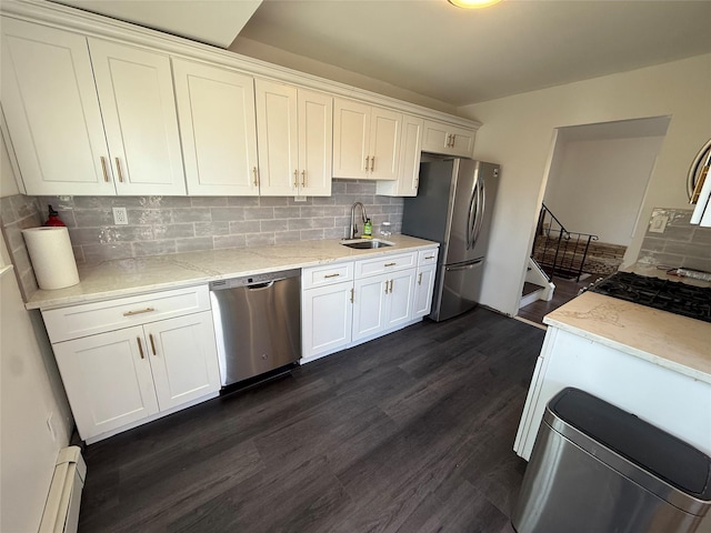 kitchen featuring white cabinets, a sink, a baseboard heating unit, decorative backsplash, and appliances with stainless steel finishes