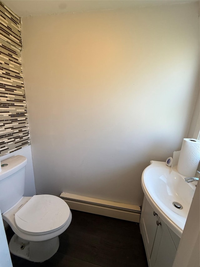 half bath featuring wood finished floors, vanity, a baseboard radiator, and toilet