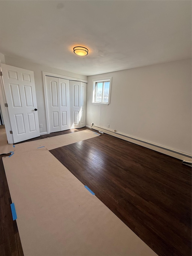 unfurnished bedroom with baseboards, baseboard heating, wood finished floors, and a closet