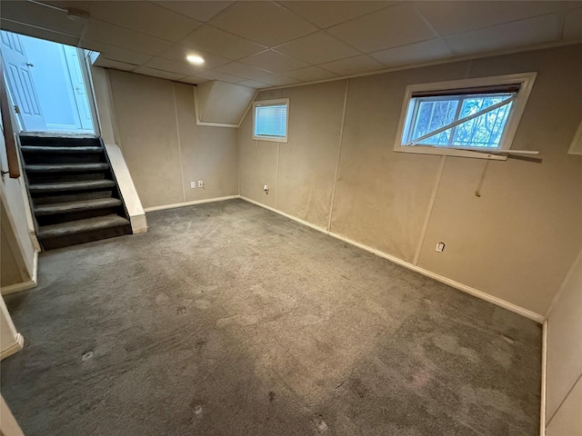 below grade area with a paneled ceiling, carpet flooring, baseboards, and stairway