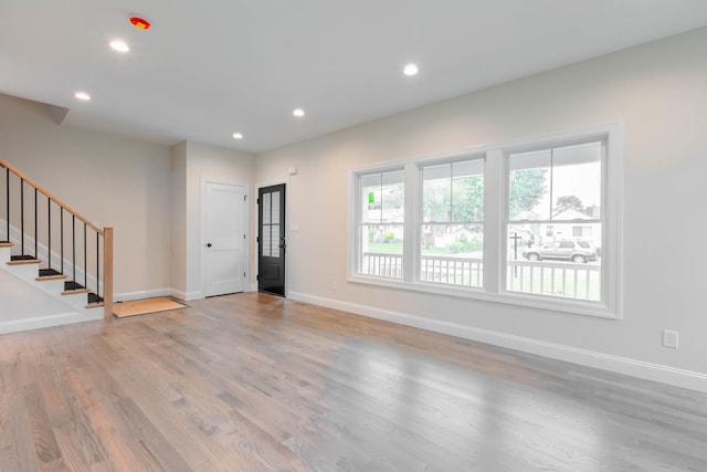 unfurnished living room with wood finished floors, baseboards, recessed lighting, and stairs