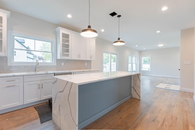 kitchen with a sink, a center island, decorative backsplash, white cabinetry, and light wood-type flooring