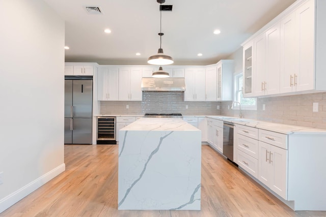 kitchen featuring appliances with stainless steel finishes, wine cooler, under cabinet range hood, a sink, and a kitchen island