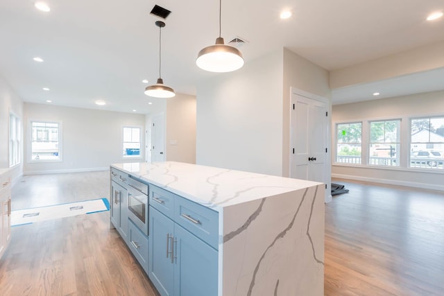 kitchen featuring open floor plan, light wood-style flooring, stainless steel microwave, decorative light fixtures, and recessed lighting